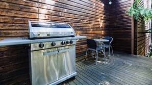 A stainless steel outdoor grill with four burners, a table, and two chairs on a wooden deck. - Warburton Lodge (Warburton)