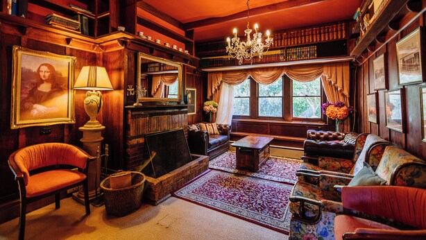 A cozy, wood-paneled room with a fireplace, plush seating, and bookshelves. - Warburton Lodge (Warburton)