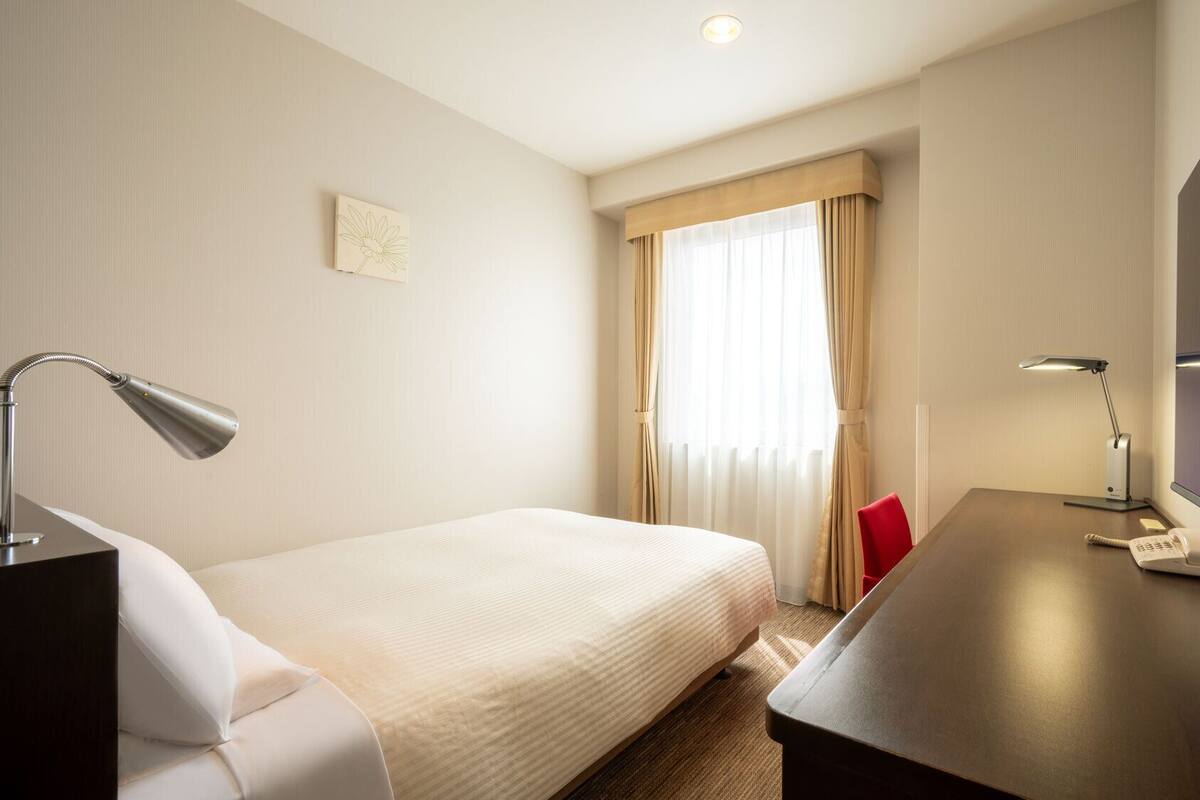 Ein Hotelzimmer mit einem Bett, einem Schreibtisch mit Lampe, einem Telefon und einem Fernseher.