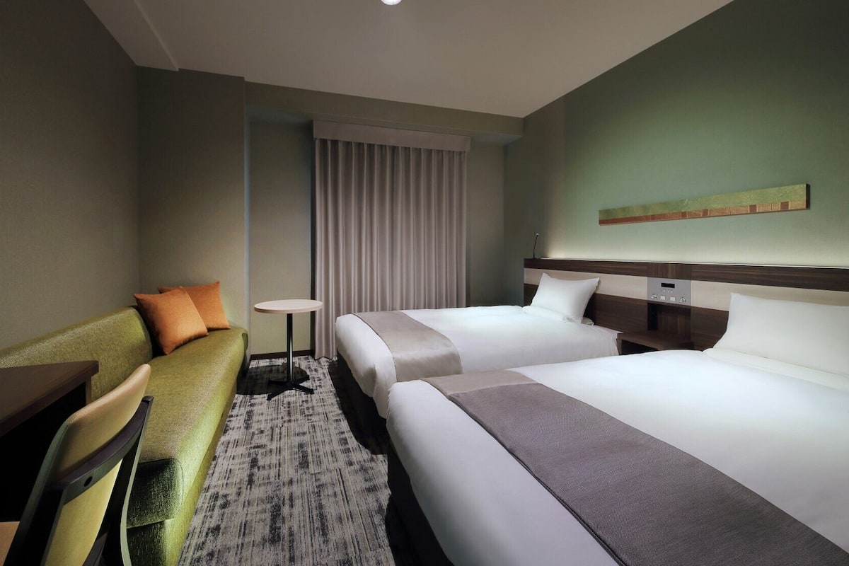Ein Hotelzimmer mit zwei Betten, einem Sofa, einem kleinen Tisch und einem Fernseher.