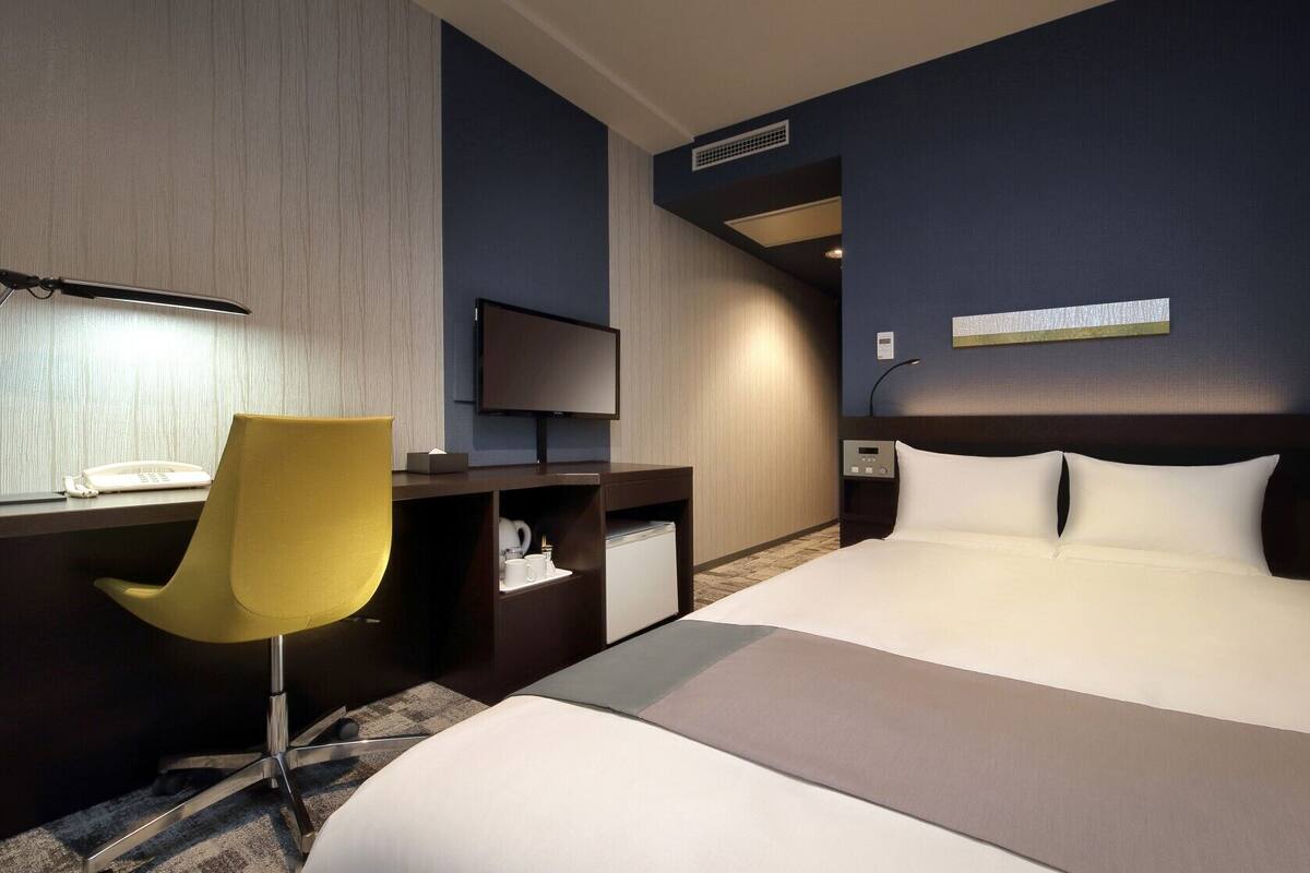 Ein modernes Hotelzimmer mit Bett, Schreibtisch, Stuhl, Fernseher und Nachttisch.