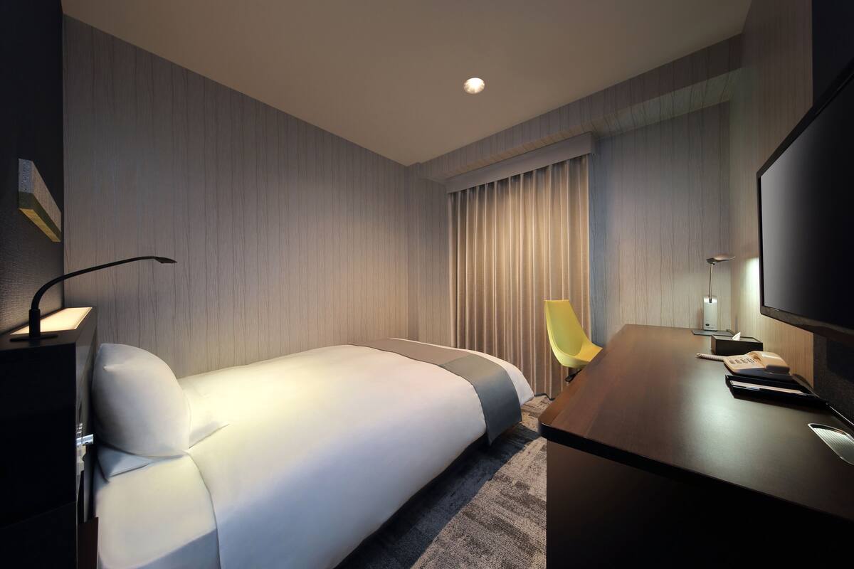 Ein modernes Hotelzimmer mit Bett, Schreibtisch, Stuhl, Fernseher und Lampe.