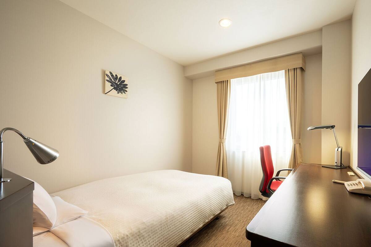 Ein Hotelzimmer mit einem Bett, einem Schreibtisch mit Computer, Telefon und Fernseher.