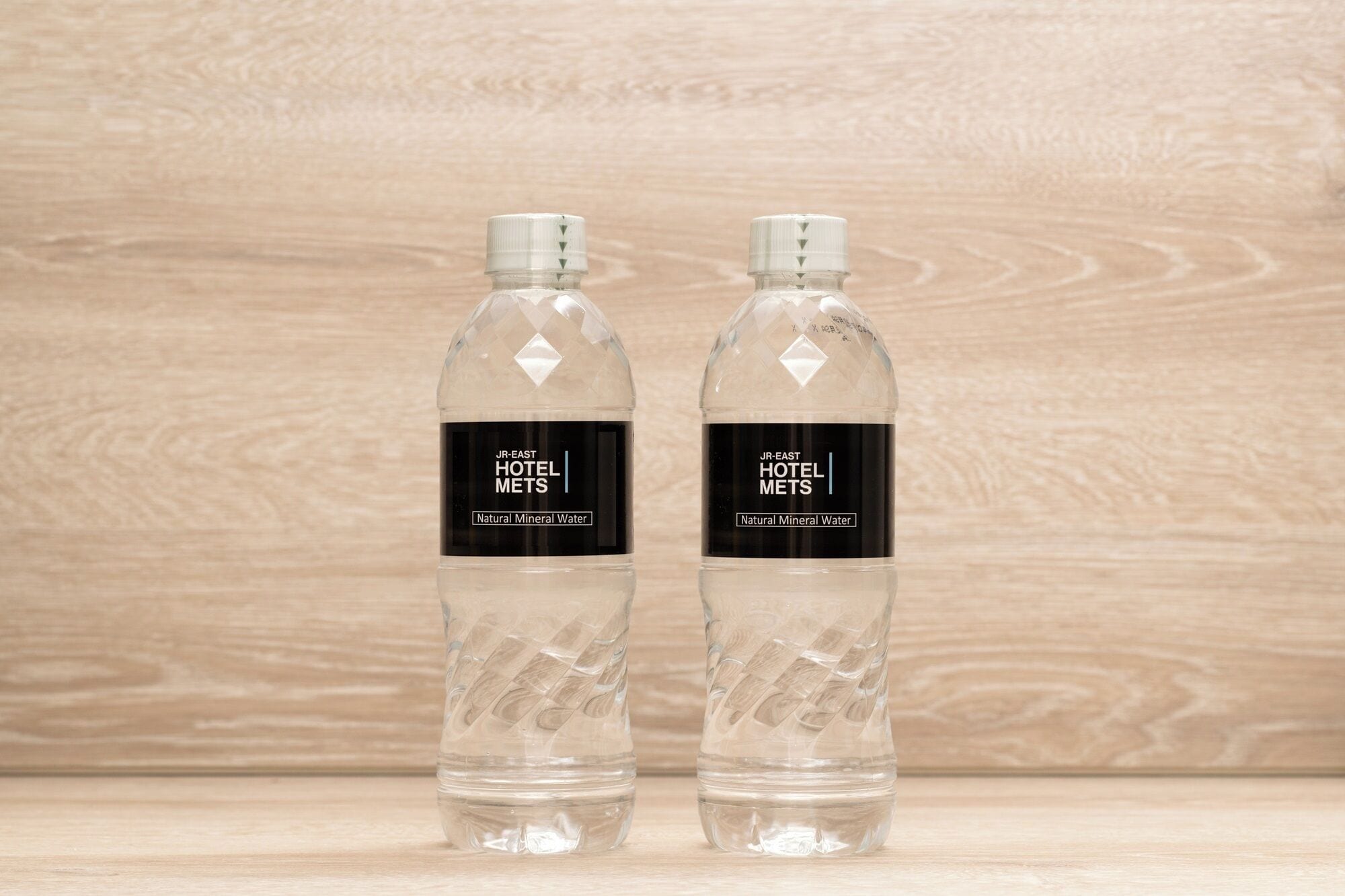 Two clear plastic bottles with labels, placed on a wooden surface against a wooden background.