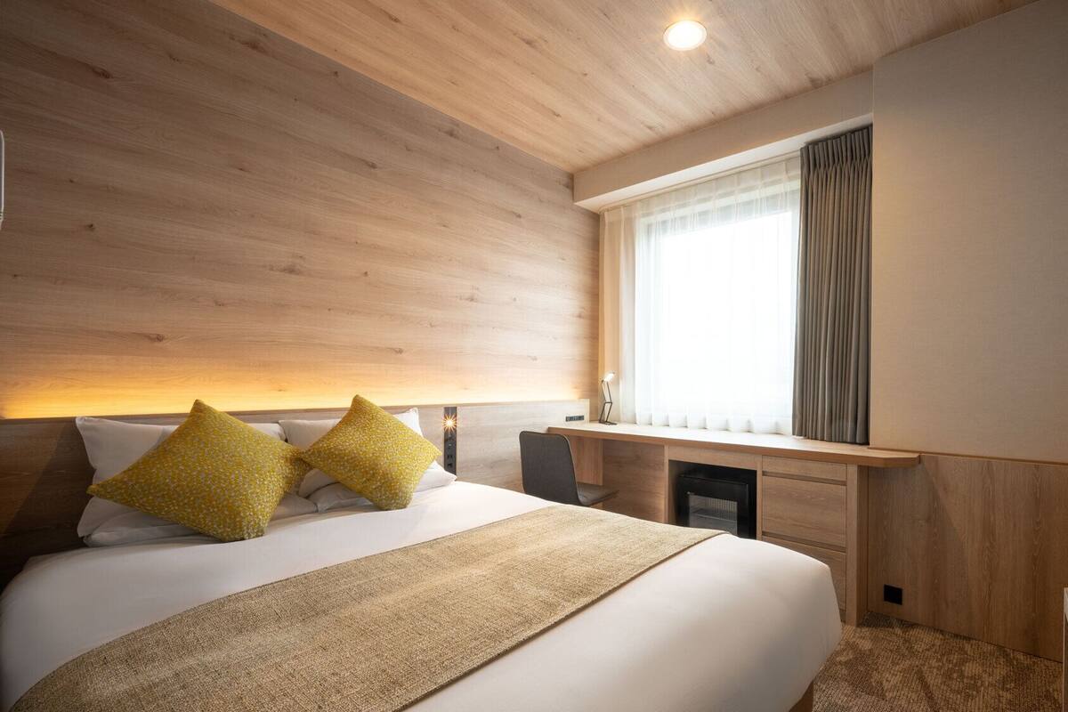 Ein Hotelzimmer mit Bett, Nachttisch, Schreibtisch und Fenster.