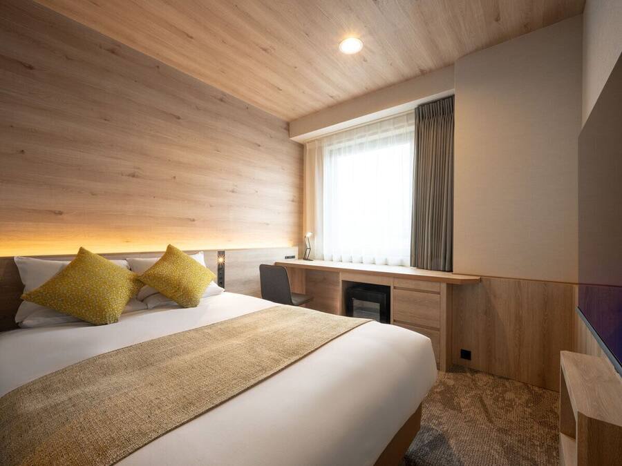 Una habitación de hotel moderna con una cama grande, un escritorio y una ventana con cortinas.