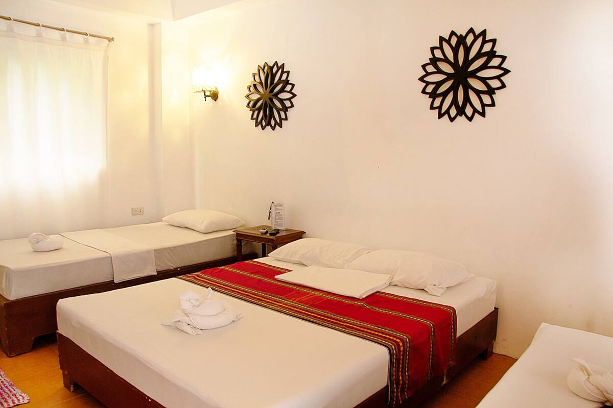 Habitación de hotel con dos camas individuales, una cubierta para la cama en rojo y dorado, ropa blanca y decoración en la pared.