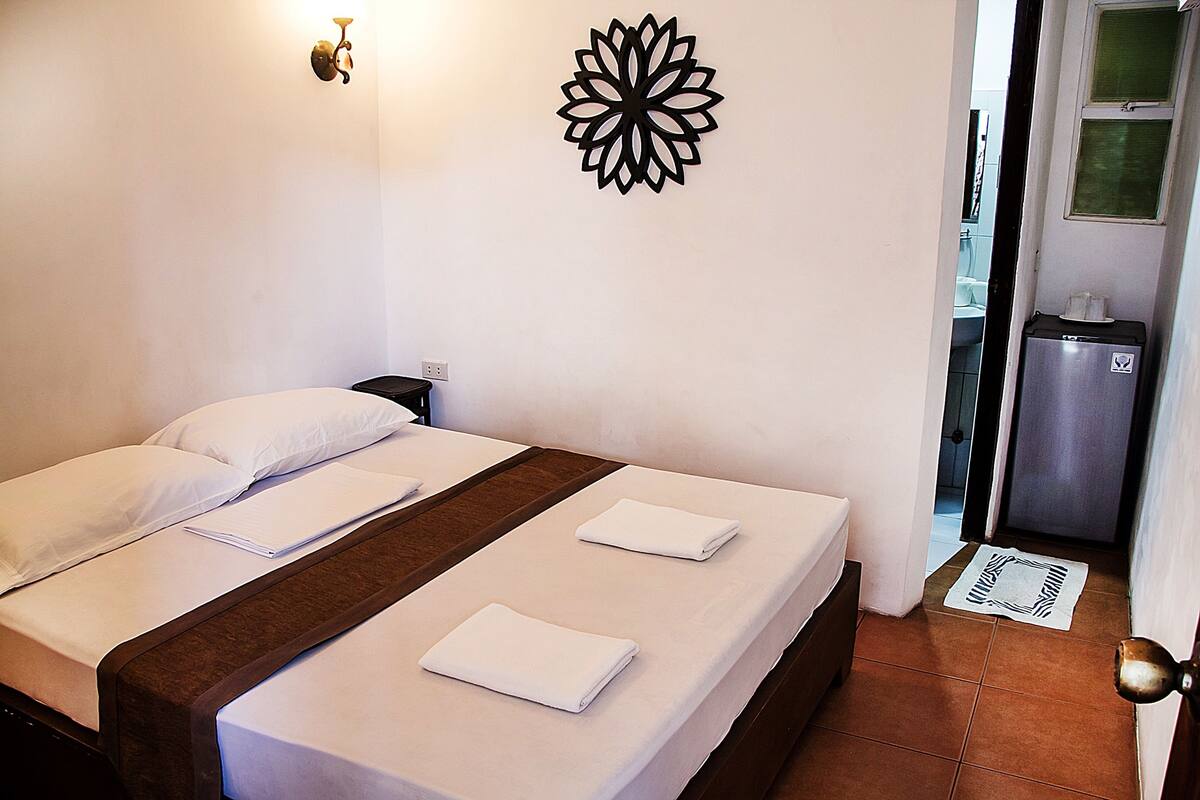 Una habitación de hotel con una cama, un adorno en la pared y un baño visible a través de una puerta abierta.