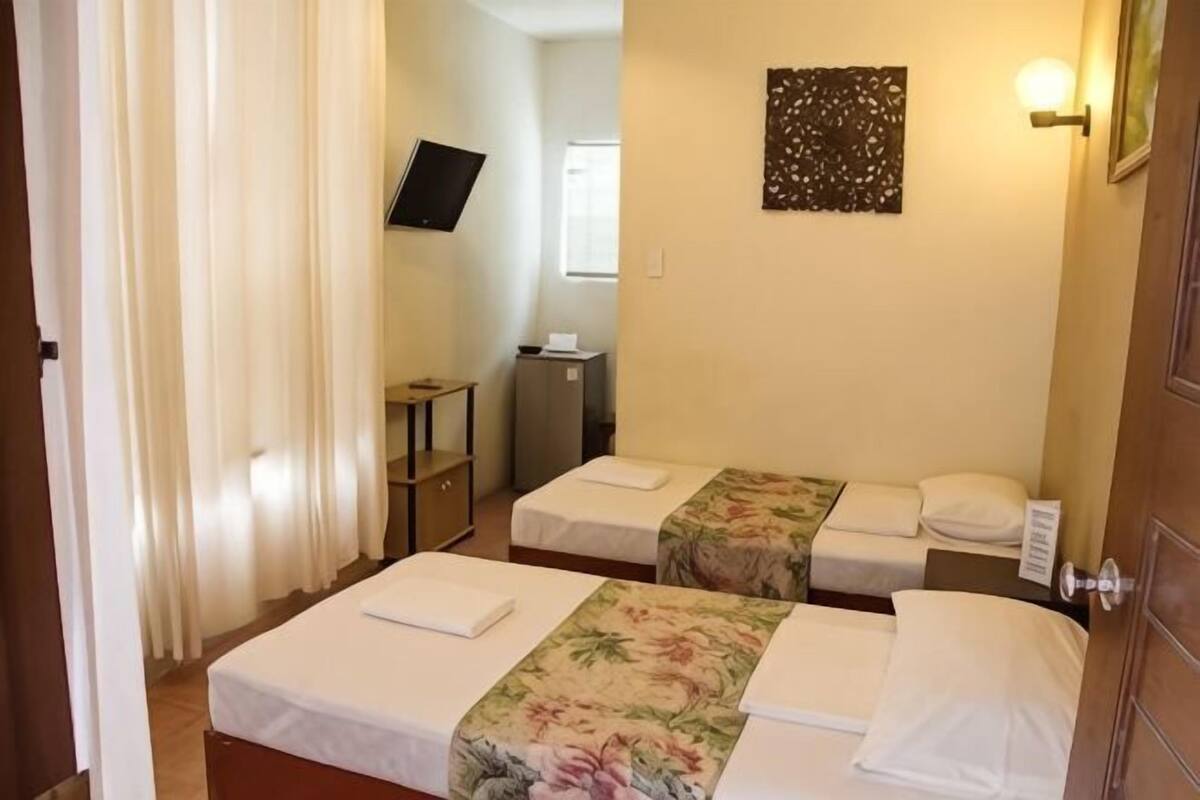Habitación de hotel con dos camas, televisión, escritorio y lámpara de pared.
