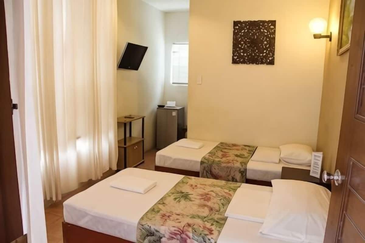 A hotel room with two beds, a TV, a desk, and a wall-mounted light fixture.