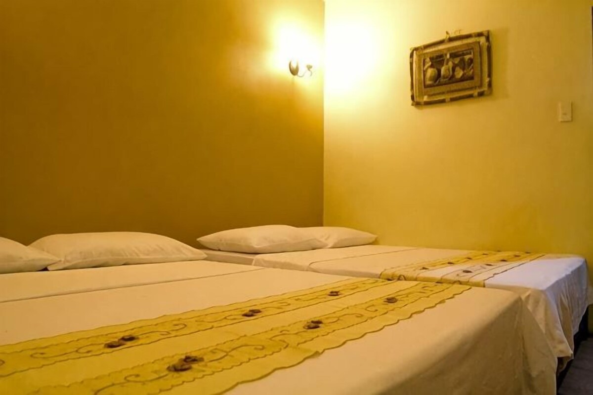 Een kamer met twee bedden, een lampje aan de muur en een prent in een lijst.