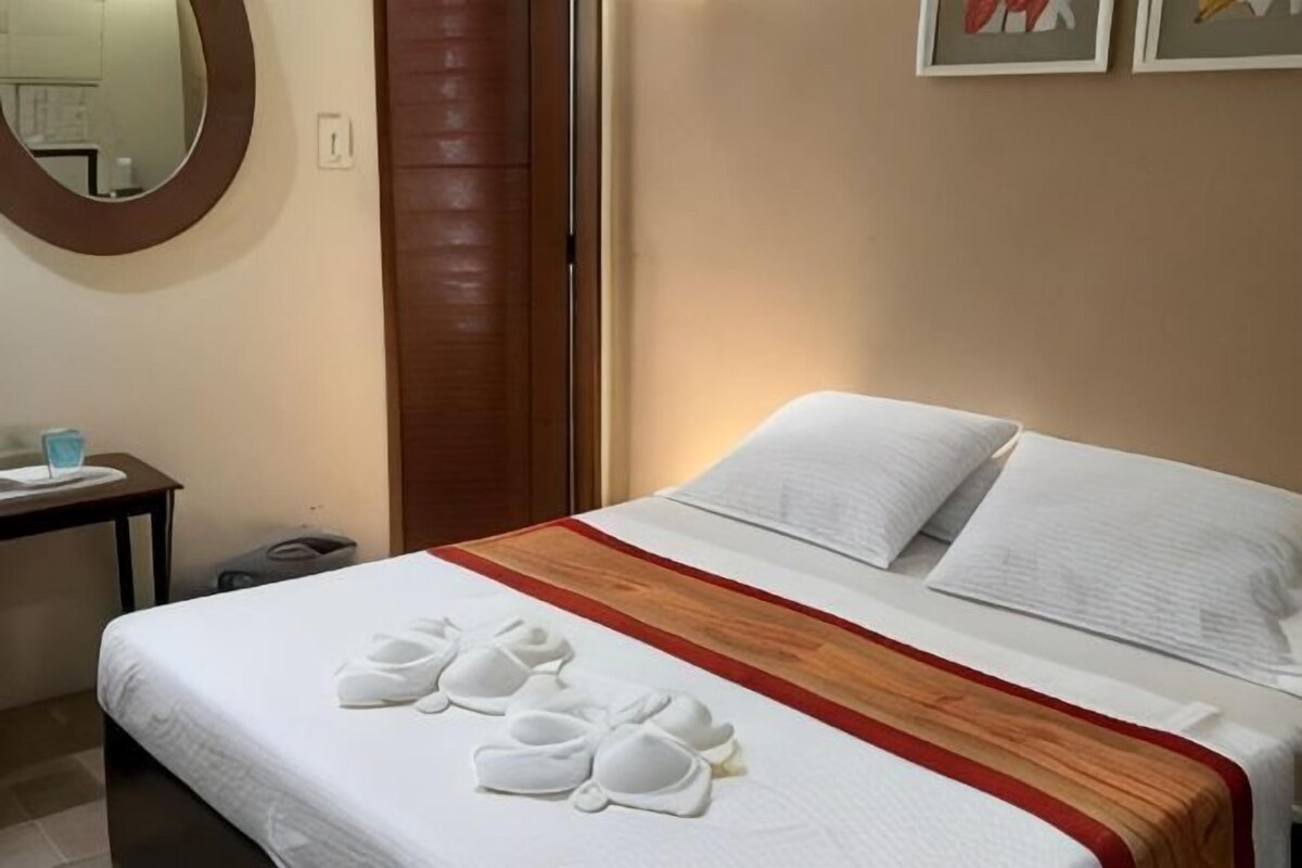 Een hotelkamer met een bed, nachtkastje, spiegel en een muur met een ingelijst kunstwerk.