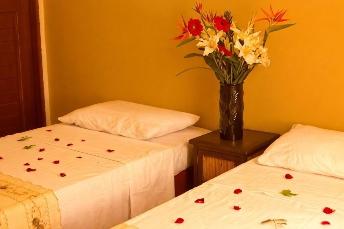 Een kamer met twee bedden, een bloemenvaas en een houten nachtkastje.