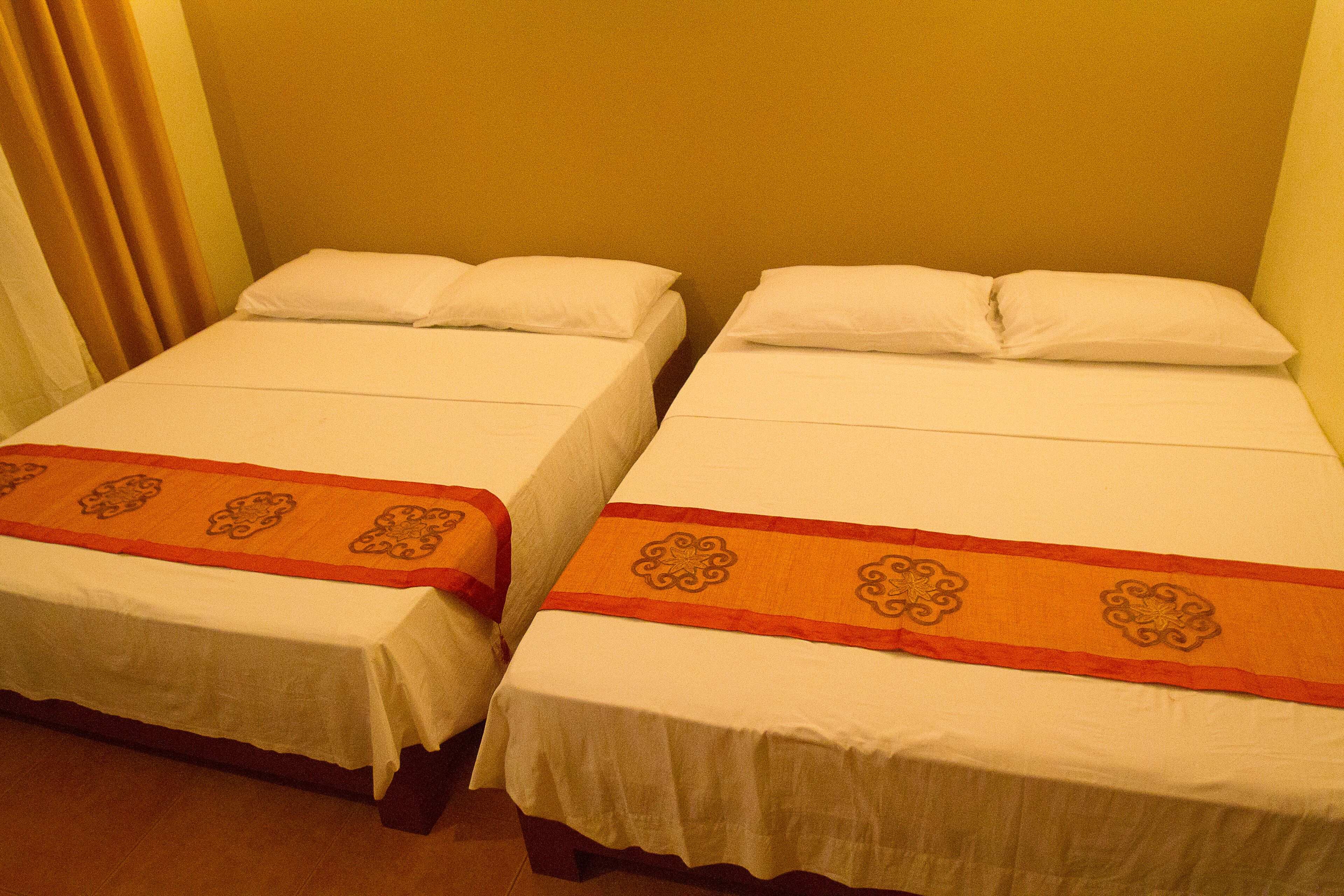 Dos camas individuales con ropa blanca y elegantes corredores decorativos anaranjados.