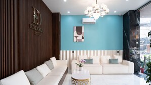A modern hotel lobby with a wooden reception desk, a white sofa, a gold-patterned coffee table, and a teal accent wall. - Eden Hue Hotel (Hue)