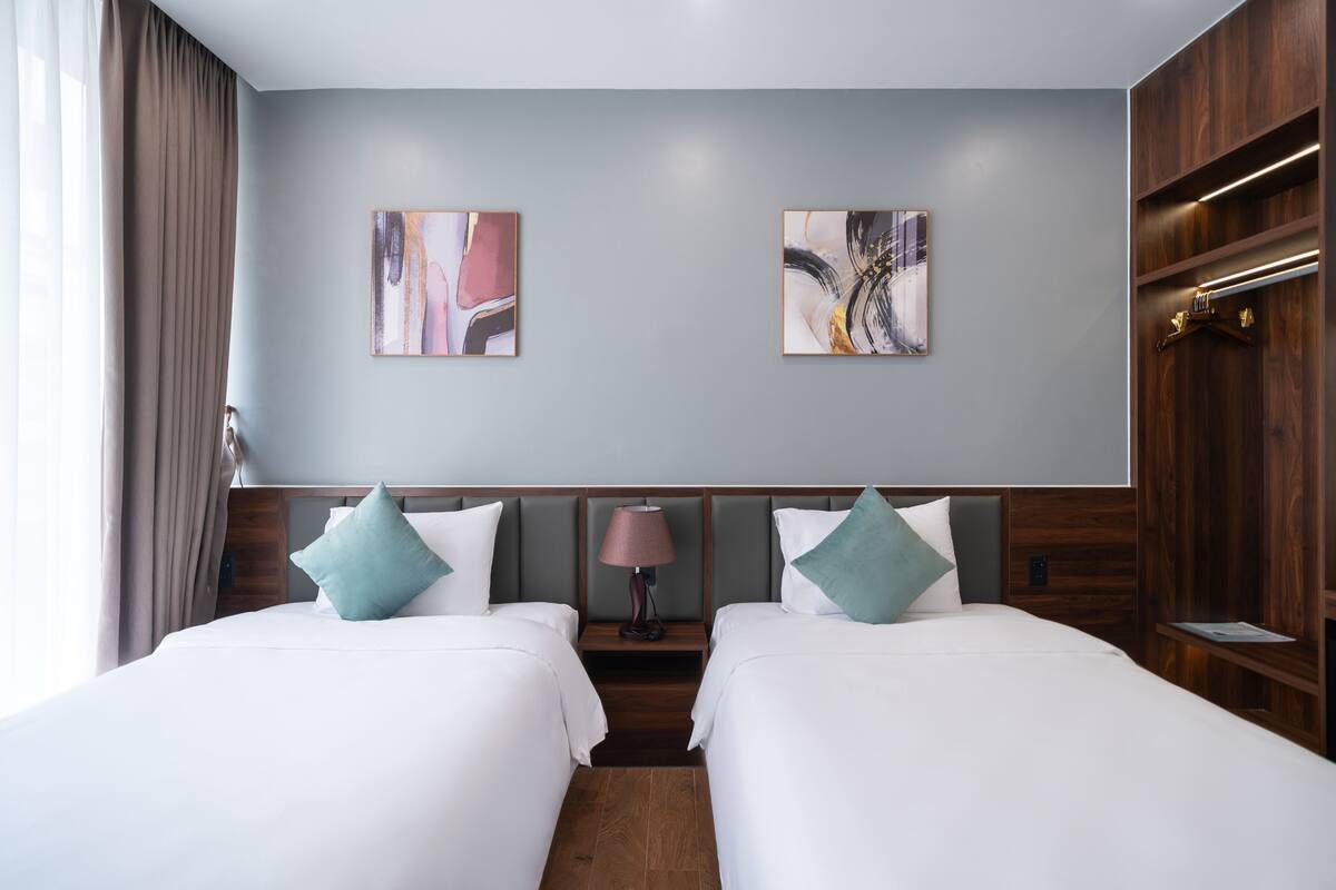 A hotel room with two beds, a wooden wardrobe, and two abstract paintings on the wall.
