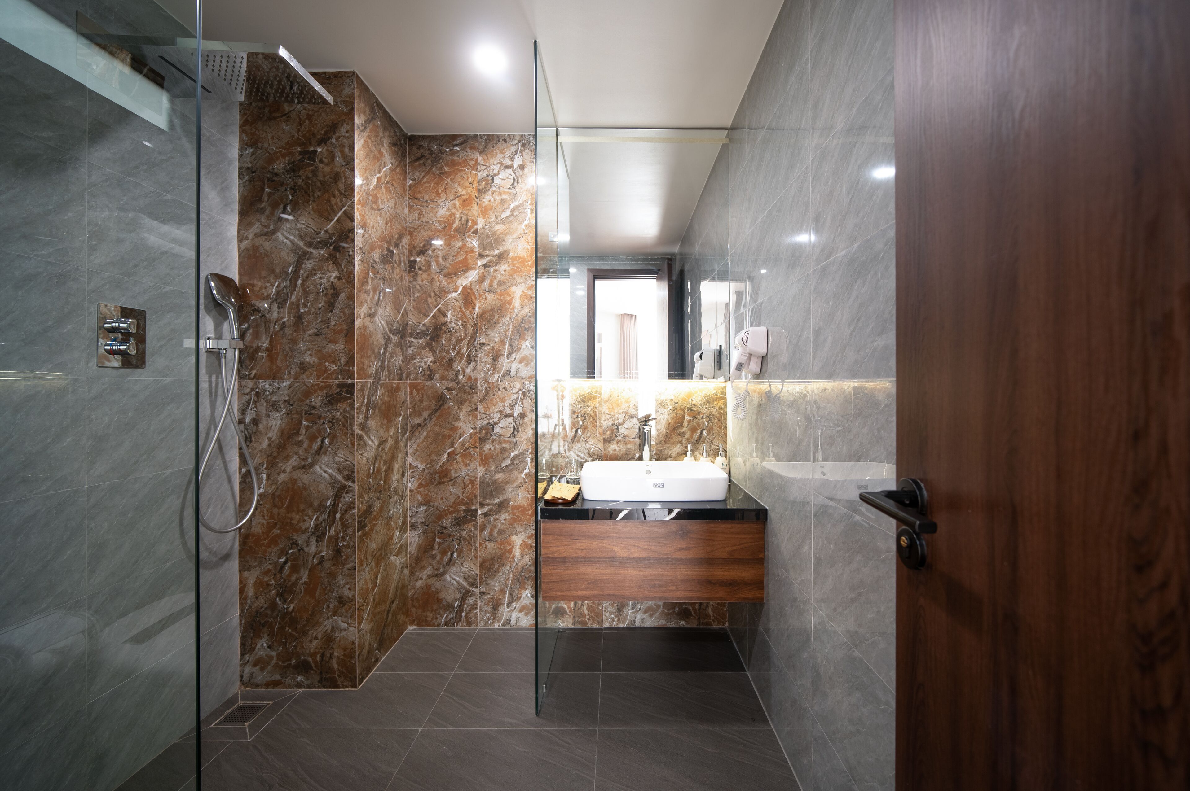Un baño moderno con cabina de ducha de vidrio, paredes de mármol y un mueble de tocador de madera con lavabo.