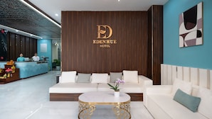 A hotel reception area with a modern design, featuring a reception desk, a seating area with sofas, and a decorative coffee table. - Eden Hue Hotel (Hue)