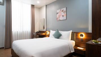 A modern hotel room with a large bed, a bedside table with a lamp, a mirror, and a wall-mounted light fixture.