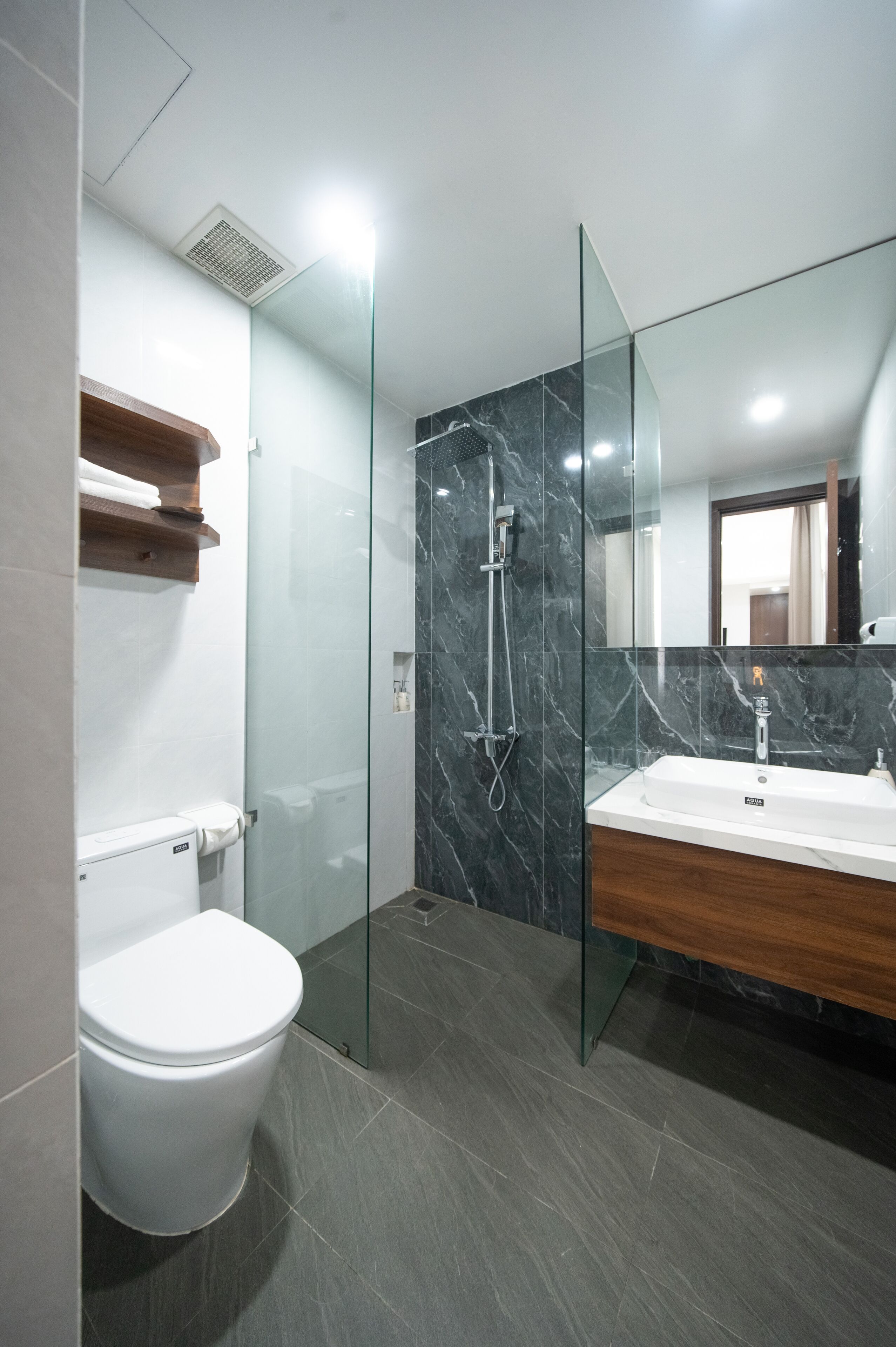 A modern bathroom with a glass-enclosed shower, a white toilet, and a wooden vanity with a sink.