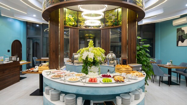 A modern breakfast buffet with a central floral arrangement, surrounded by various food items and seating areas. - Eden Hue Hotel (Hue)