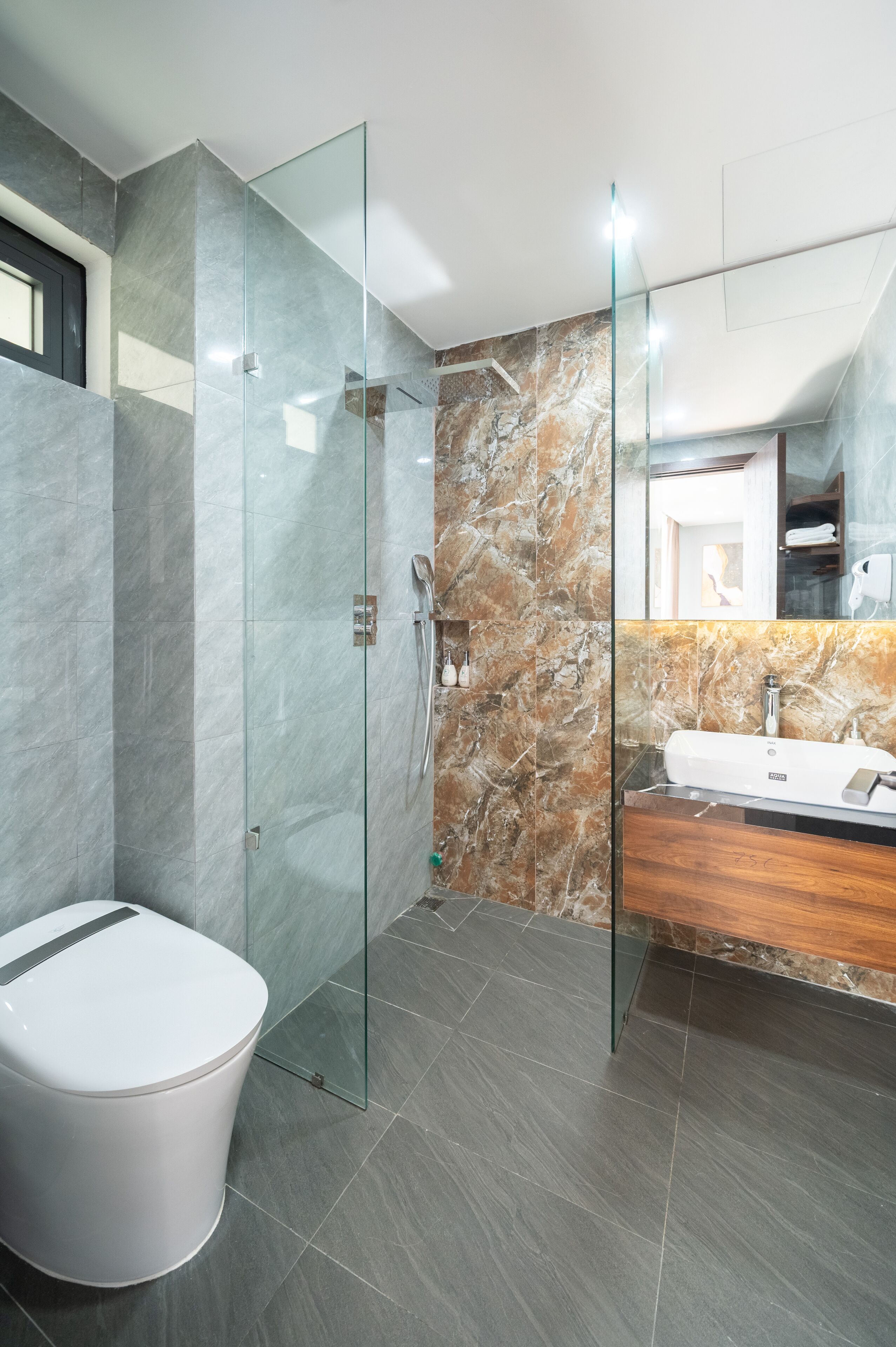A modern bathroom with a glass-enclosed shower, a marble-tiled wall, and a wooden vanity.
