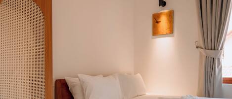 A neatly arranged bedroom with a bed, a wooden nightstand, a small stool, and a wall-mounted light fixture.