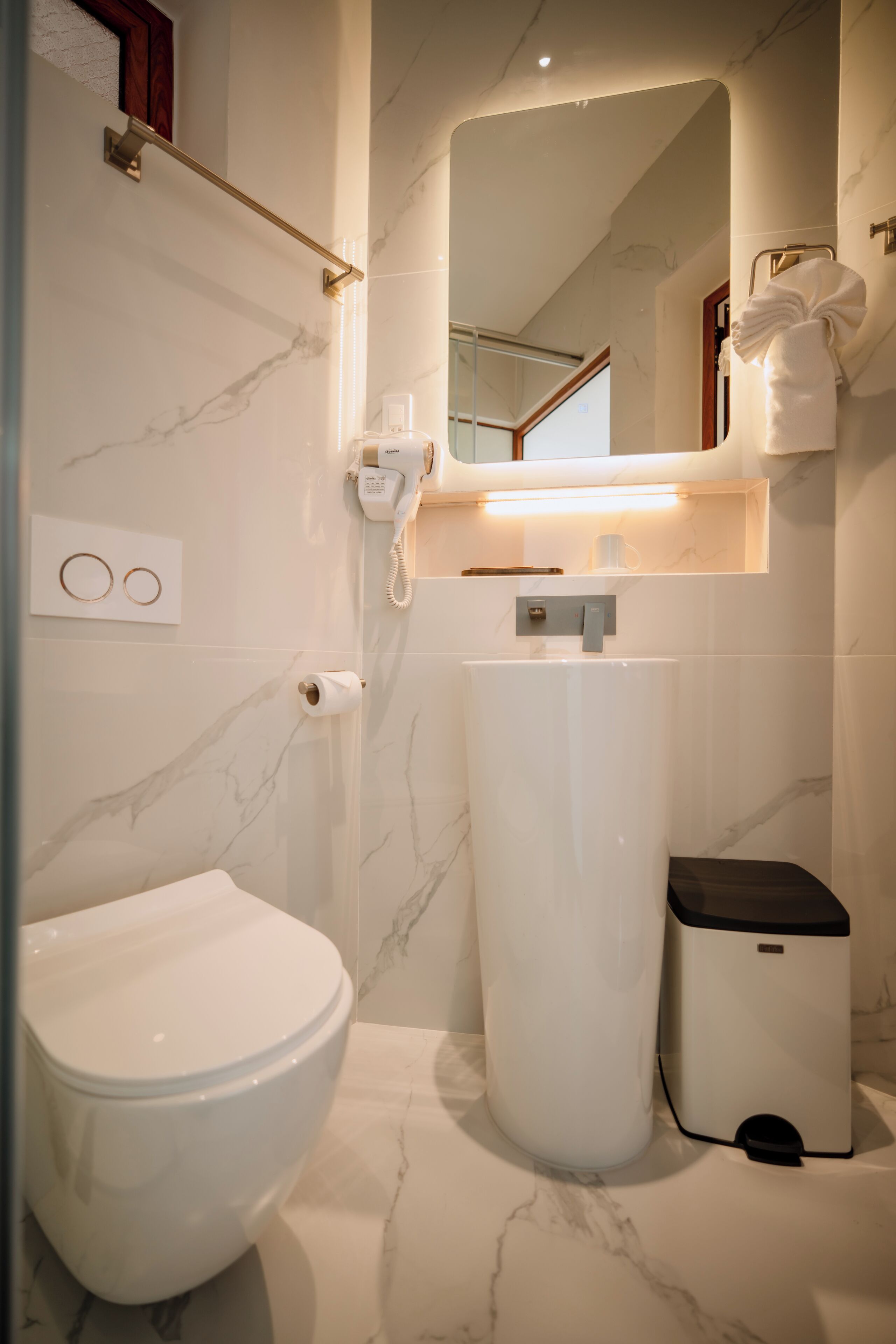 A bathroom with a toilet, a large sink, and a trash can.