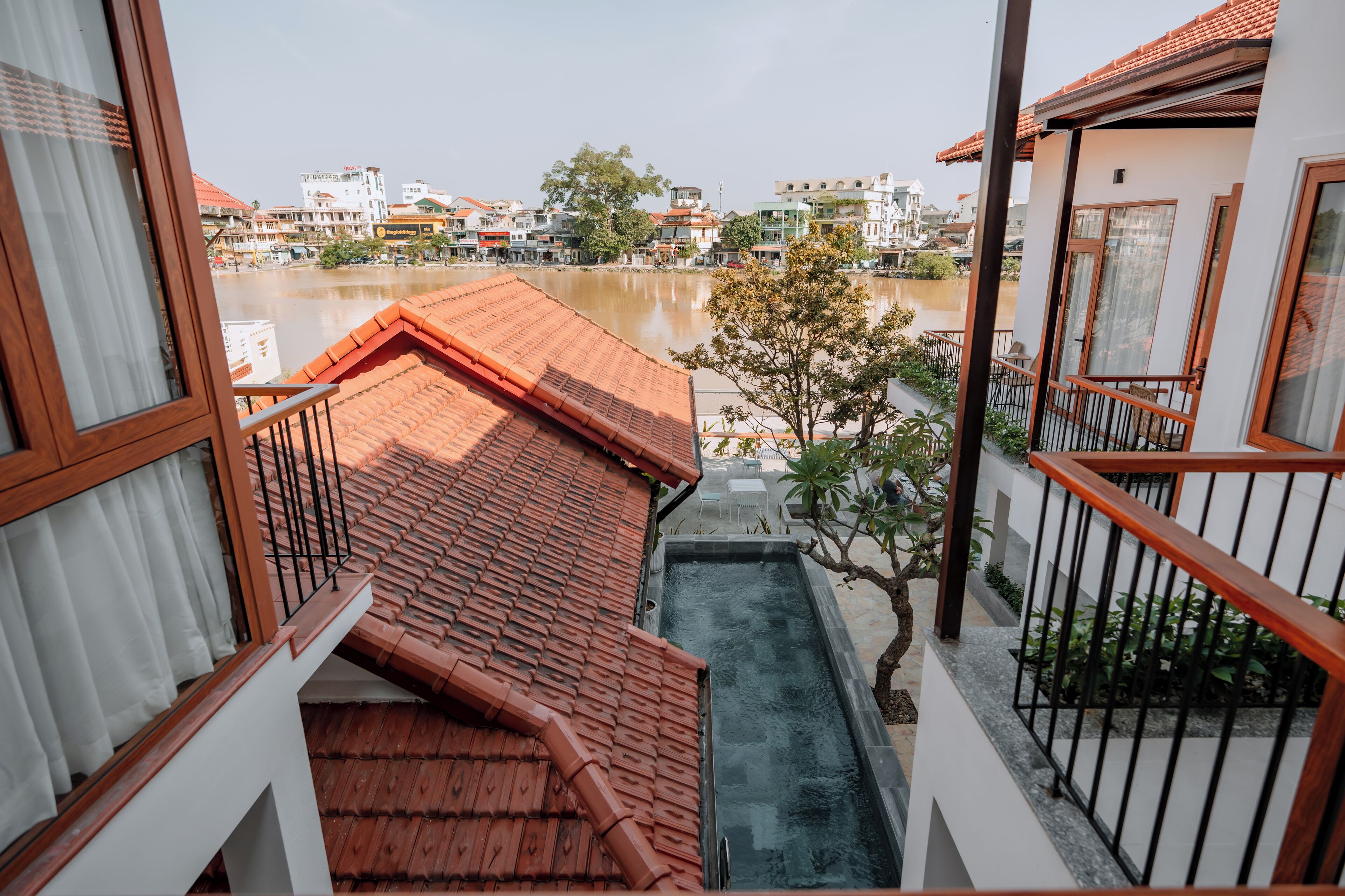 Une vue depuis un balcon donnant sur une rivière, avec des bâtiments et un arbre en arrière-plan.