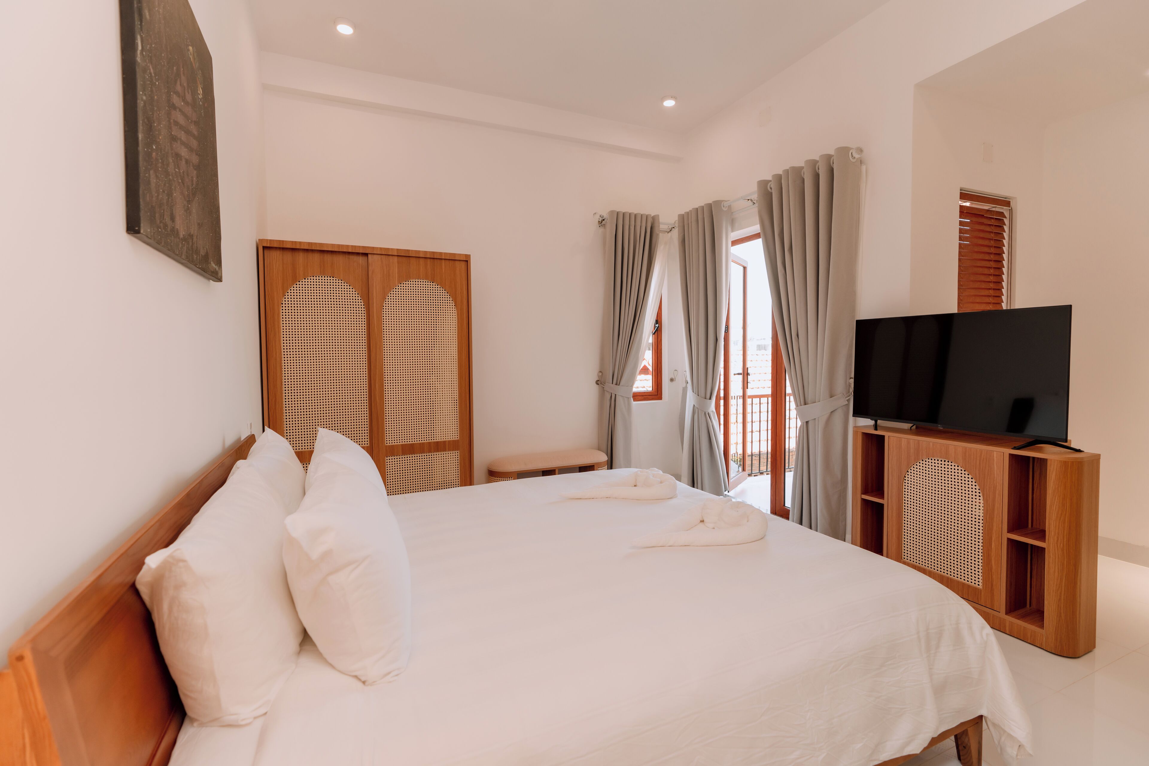 A hotel room with a bed, a television on a wooden stand, a wardrobe, and a window with curtains.