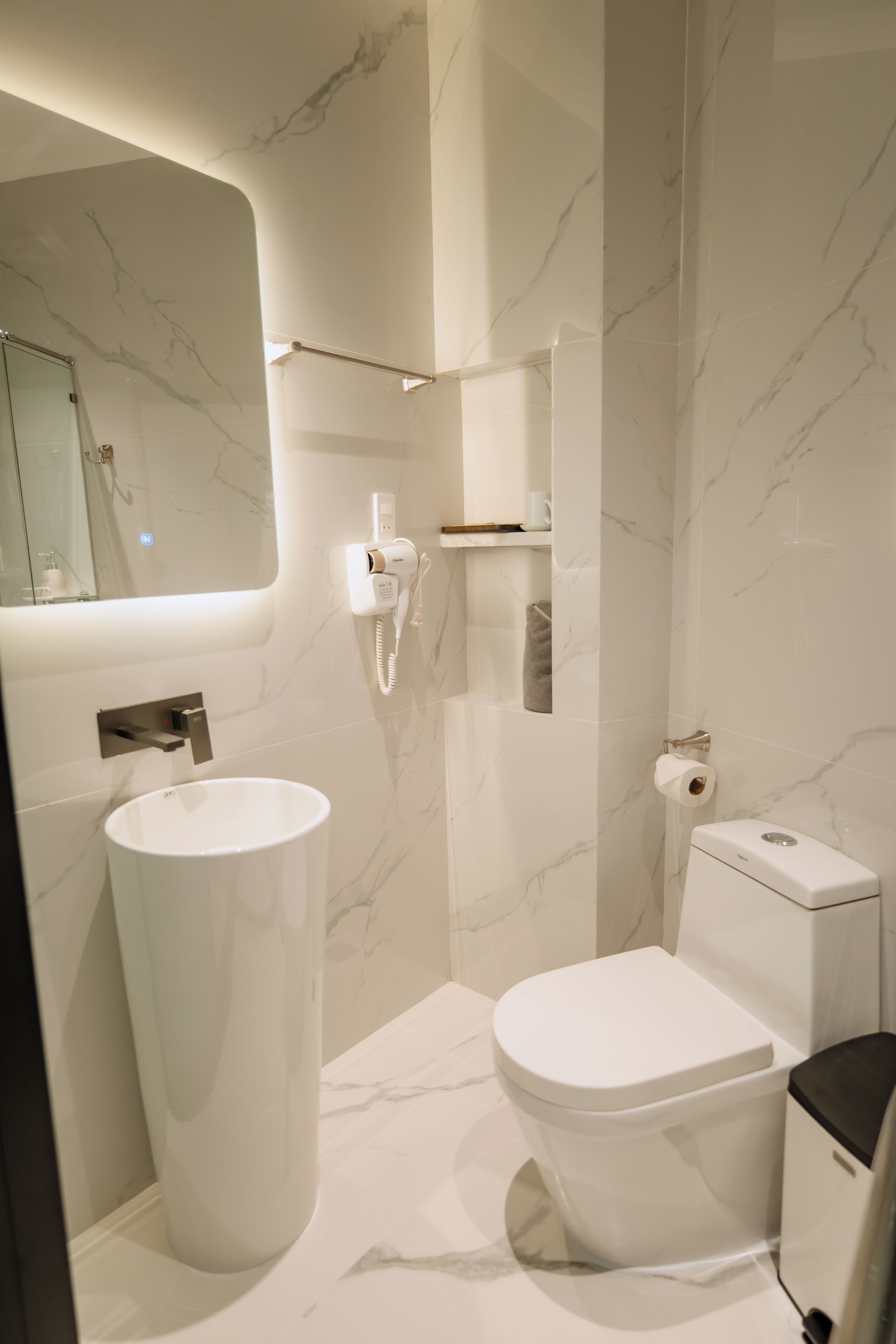 A modern bathroom with a marble wall, a white sink, a toilet, and a mirror.