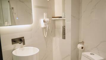 A modern bathroom with a marble wall, a white sink, a toilet, and a mirror.