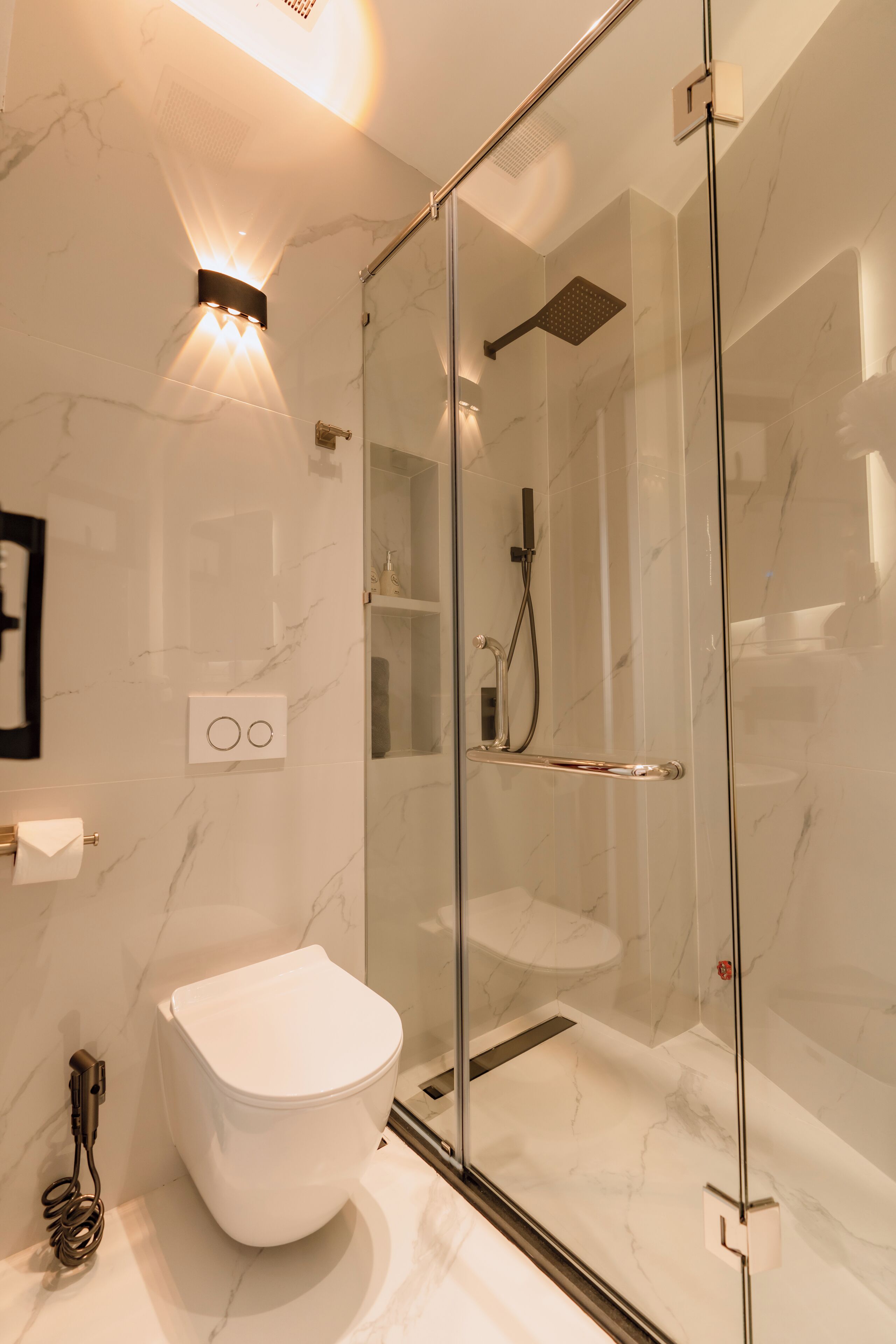 Un baño moderno con ducha envuelta en vidrio, inodoro blanco y pared revestida de mármol.