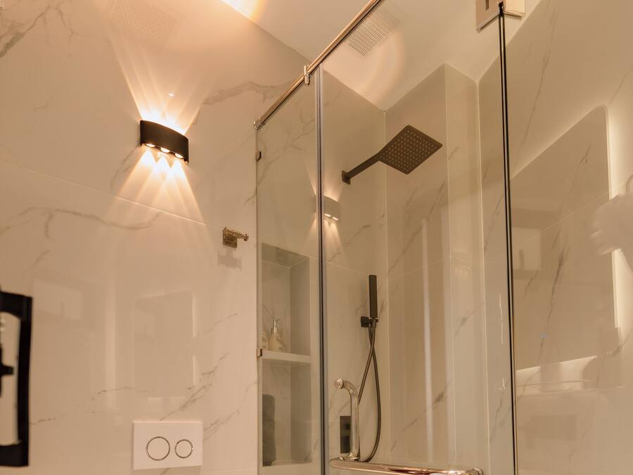 Un baño moderno con ducha envuelta en vidrio, inodoro blanco y pared revestida de mármol.