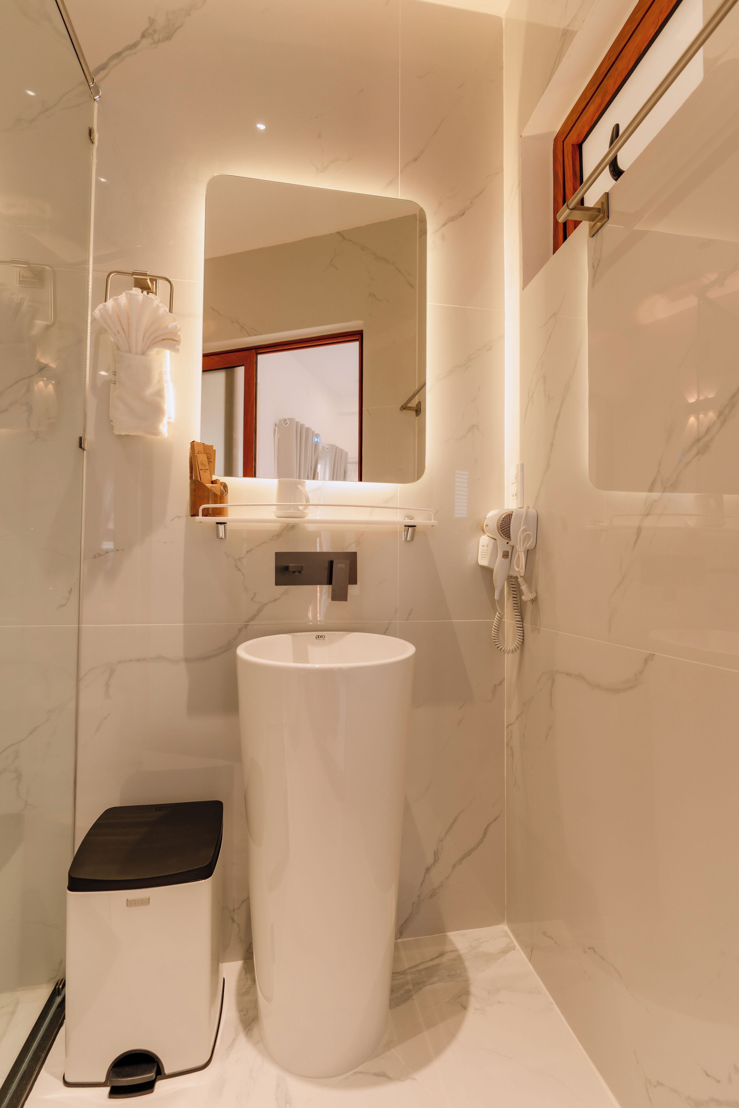 Une salle de bain moderne avec un mur en marbre, un lavabo blanc, un porte-serviettes et un miroir.