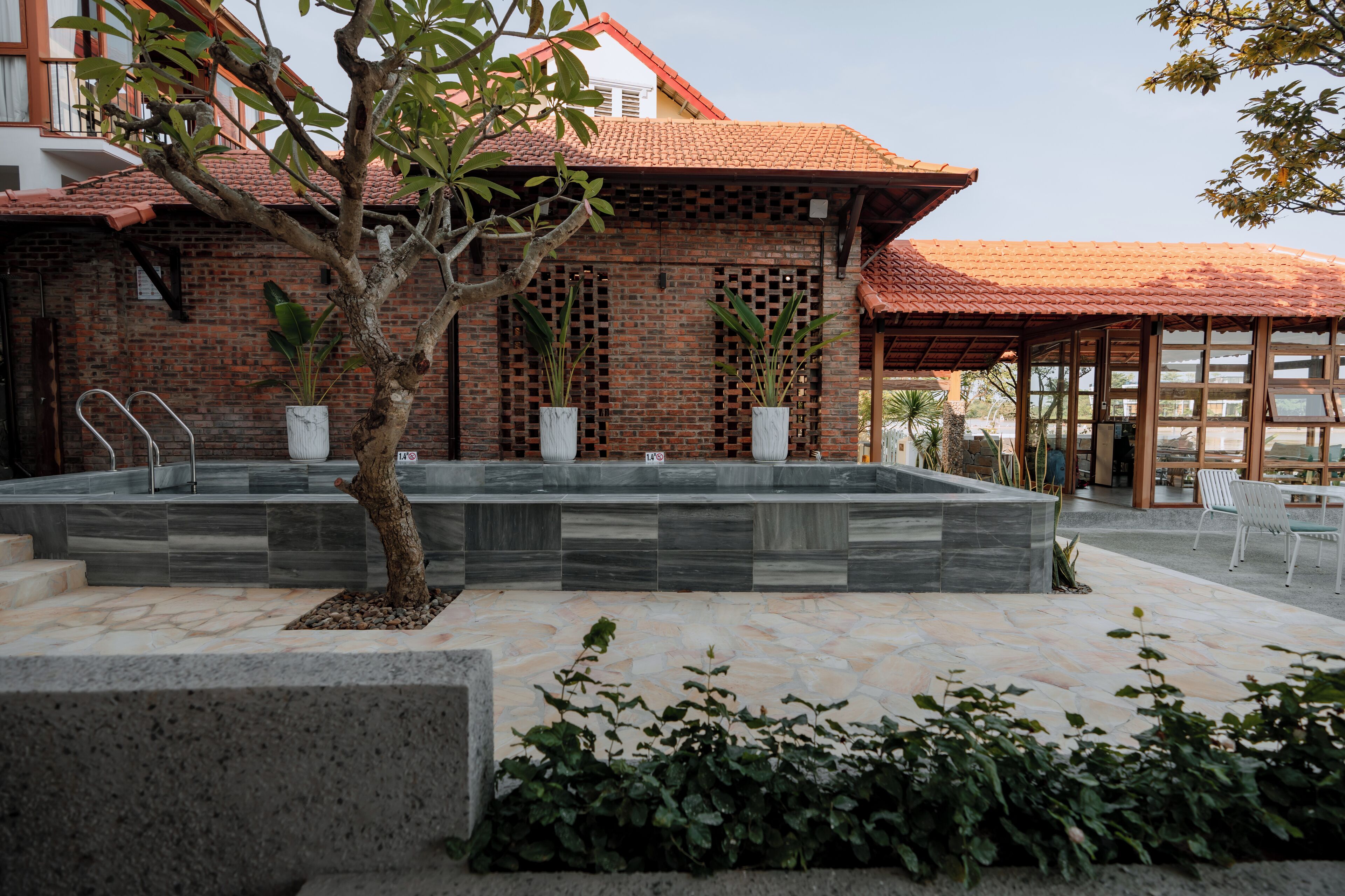 A brick building with a tiled roof, a stone pool, and outdoor seating.