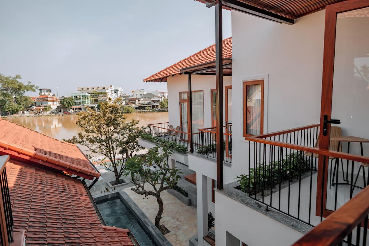 Um edifício moderno com telhado de telhas vermelhas, varanda com guarda-corpo e vista para um rio.