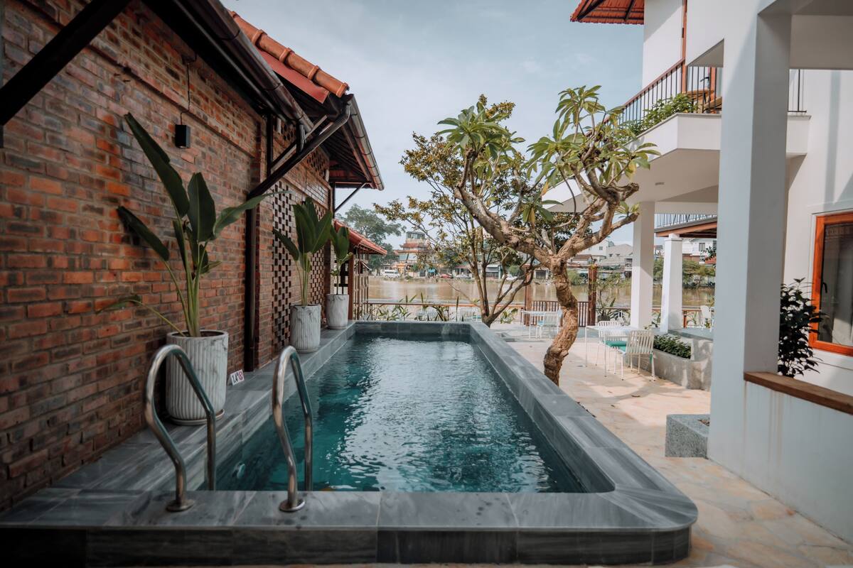 Área de piscina com parede de tijolos, plantas em vasos e vista de um edifício tradicional ao fundo.