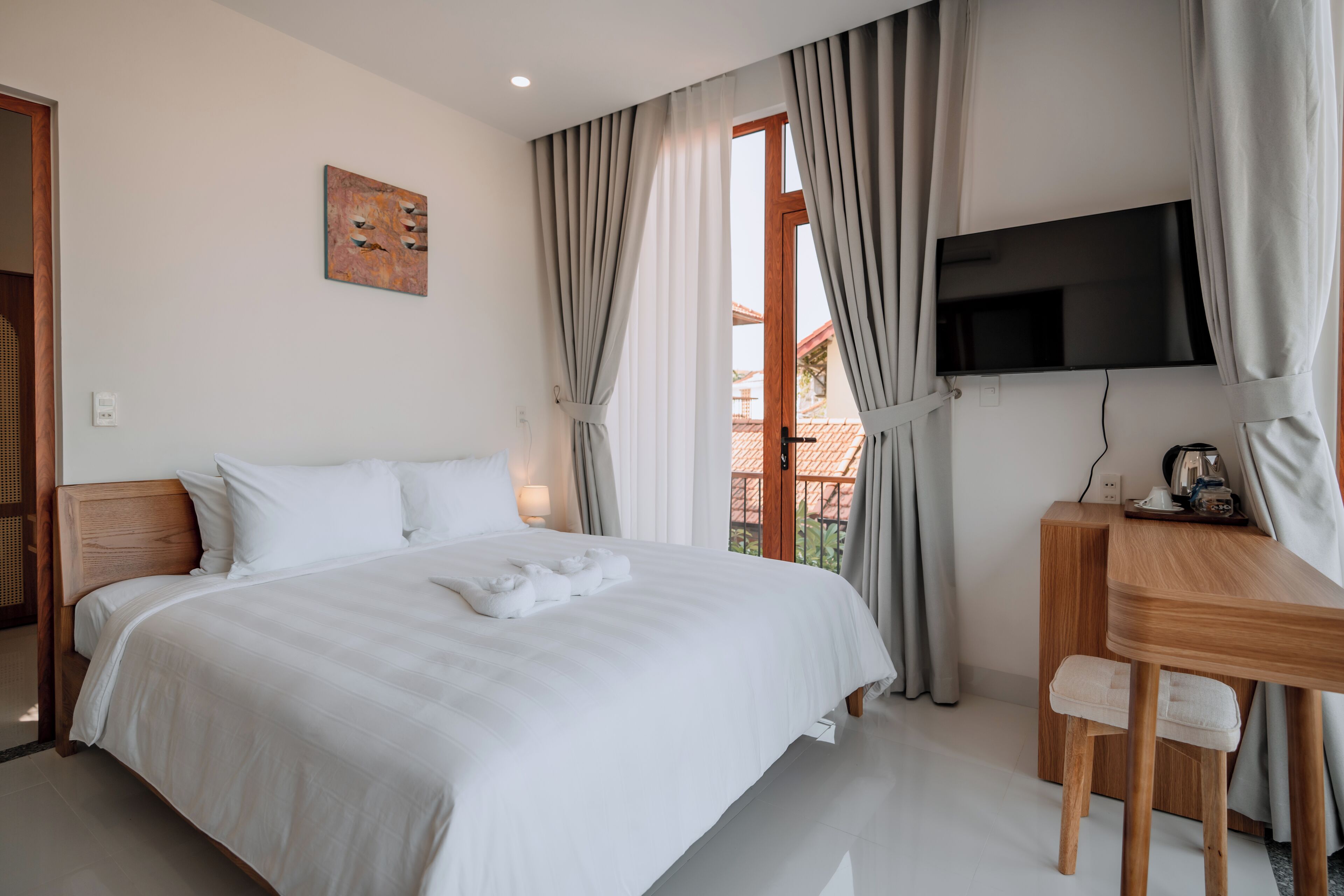 Quarto de hotel com uma cama grande, uma escrivaninha, uma TV e vista para o exterior.
