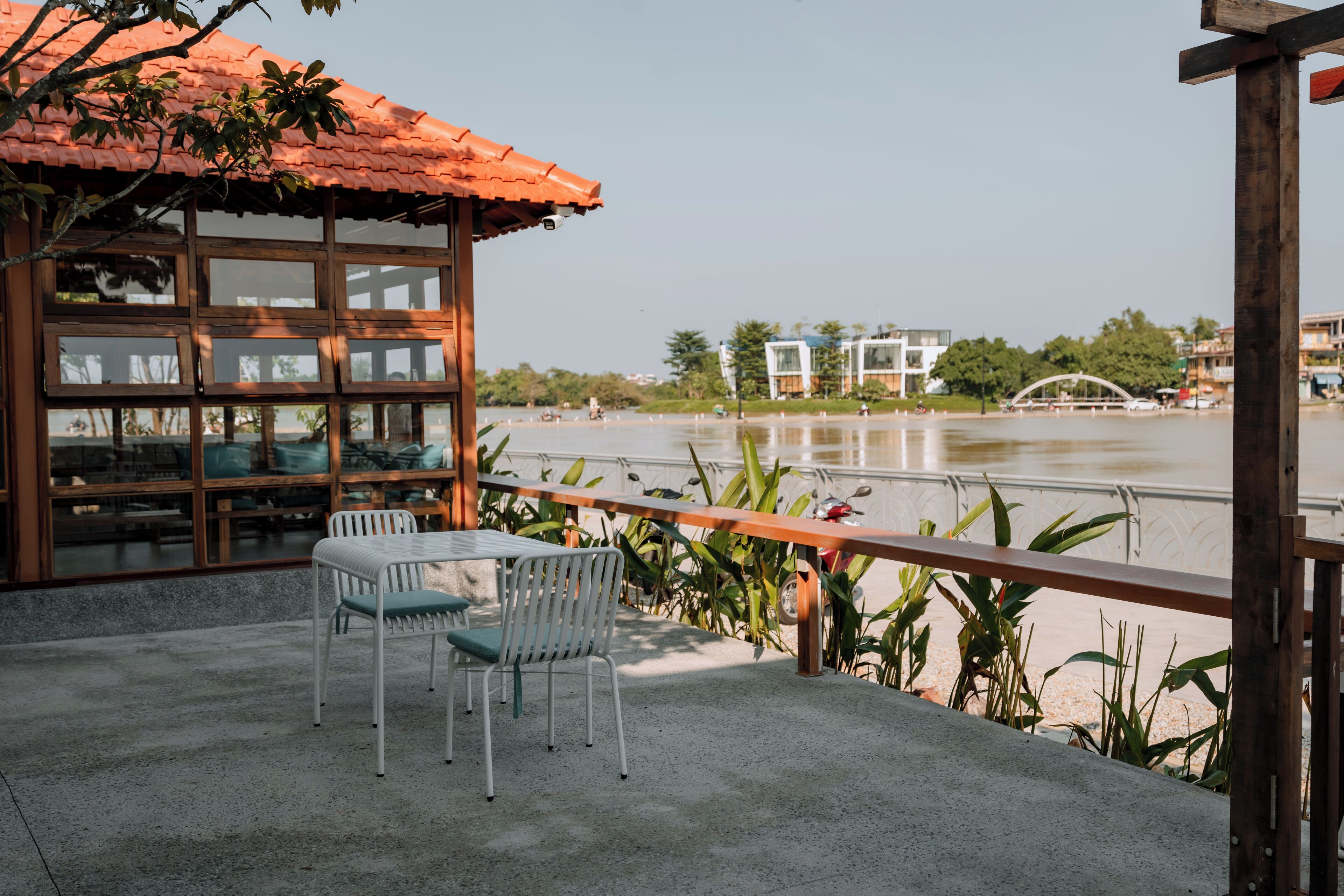 Une terrasse avec une table et des chaises, donnant sur une rivière, avec des bâtiments en arrière-plan.