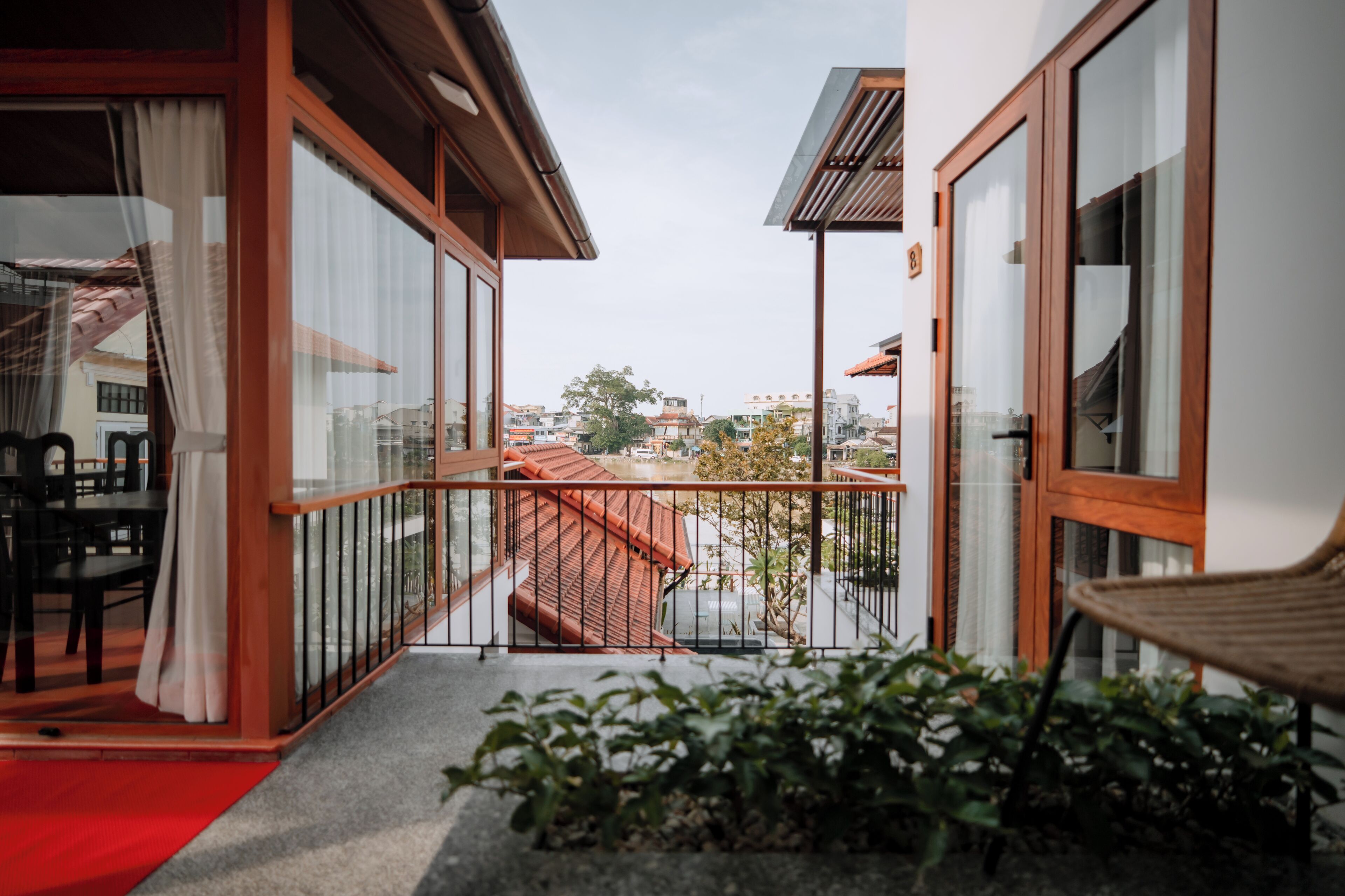 A balcony with a red carpet, a wooden chair, and a view of the cityscape.