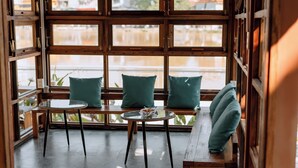 A cozy seating area with wooden benches and tables, large windows with wooden frames, and a view of the outdoors. - Hue Riverside Villa (Hue)