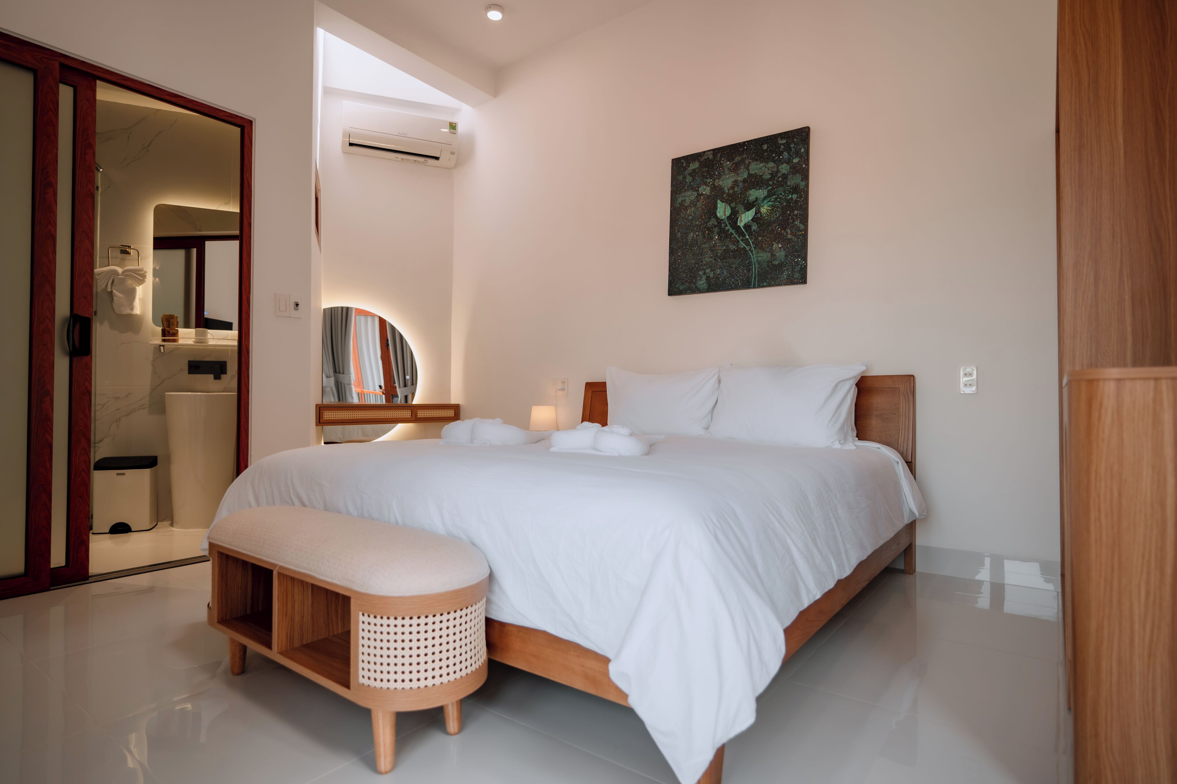 A modern bedroom with a large bed, a bedside table, a bench, and a wall-mounted air conditioner.