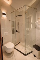 A modern bathroom with a glass-enclosed shower, a white toilet, and a bidet.