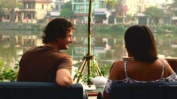 Due persone sedute vicino a una finestra con vista su un lago e edifici sullo sfondo.