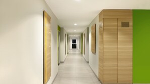 A modern hallway with wooden lockers and green accents, leading to a room with a bed and a nightstand. - Amaris Hotel Padang (Padang)