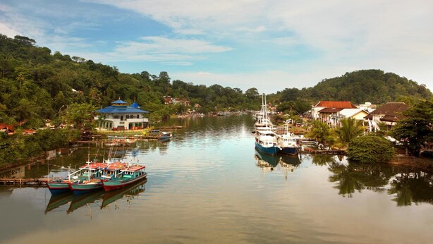 A river with boats docked, surrounded by lush greenery and buildings. - Amaris Hotel Padang (Padang)