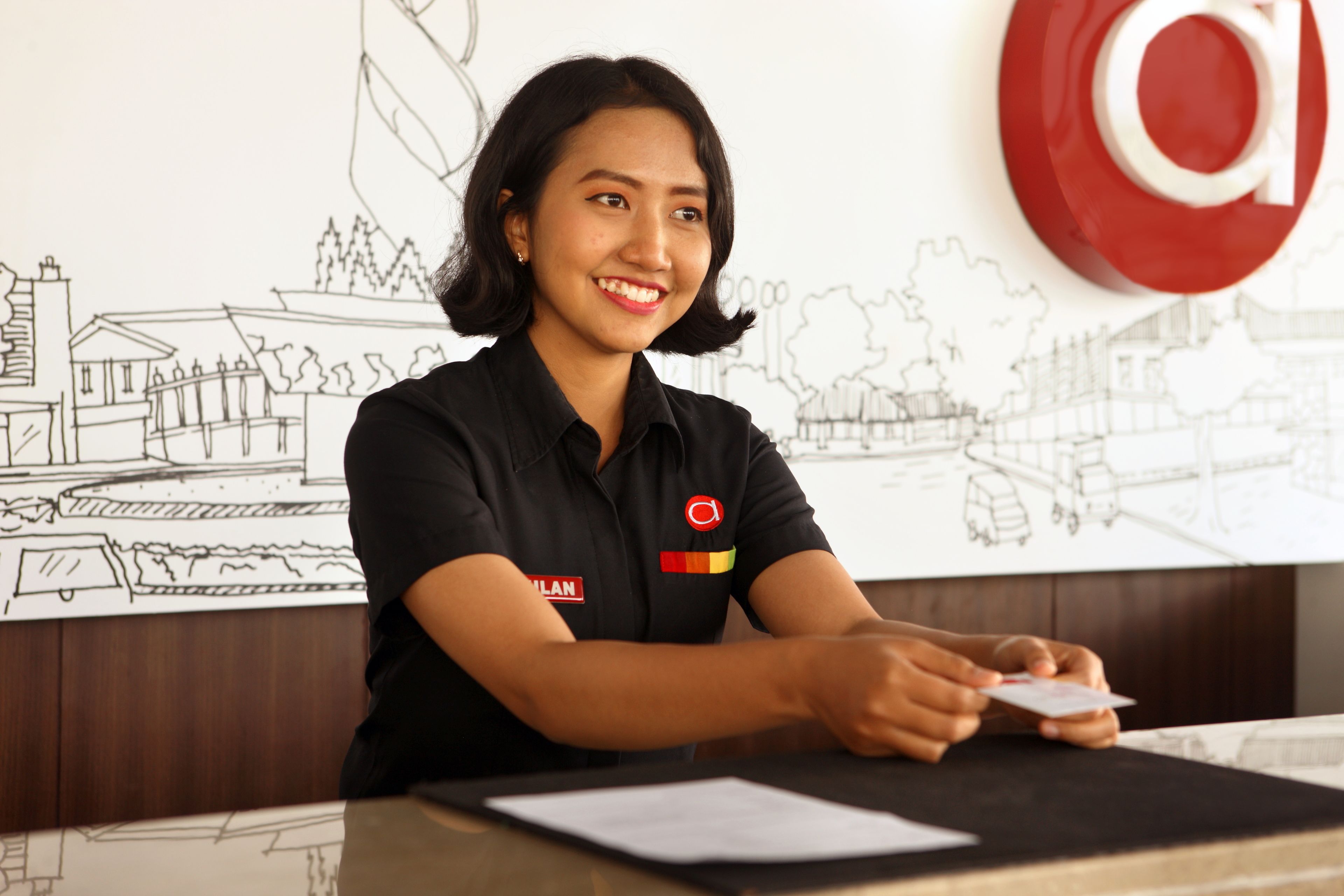 A person seated at a desk with a black shirt and a logo on the left side.