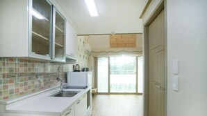 A kitchen with a tiled backsplash, a sink, cabinets, and a window with a view of the outdoors. - Olleh House (Seogwipo)