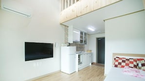 A compact room with a bed, a TV mounted on the wall, a small kitchenette, and a wooden ceiling. - Olleh House (Seogwipo)